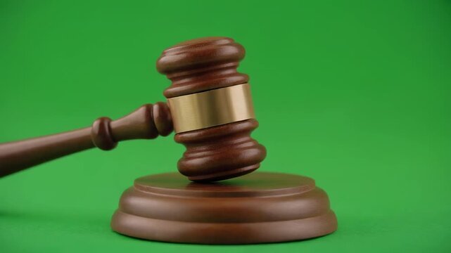 Wooden gavel striking sound block against vibrant green background for legal proceedings or auction