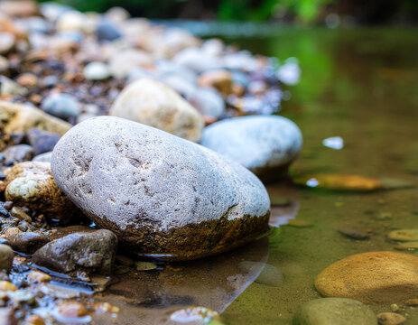 smooth round stones and pebbles along the shallow edge of a clear flowing river stream in a tranquil natural forest setting
