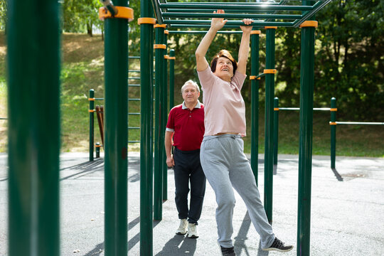 Married couple at retirement age goes in for sports on sports ground - with the help of hands they move along horizontal ladder