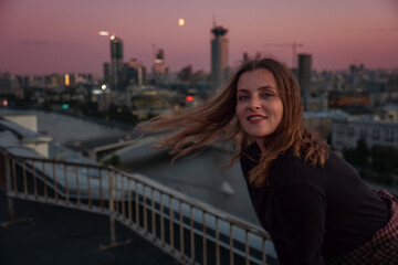 Smiling woman stands on rooftop above Zamoskvorechye district with Moscow skyline at sunset. Travel, urban lifestyle, city exploration, rooftop leisure, tourism, freedom. © Sofia
