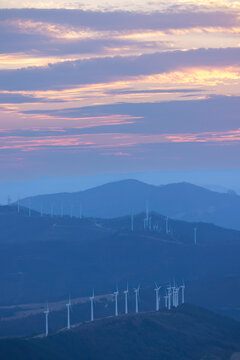 Wind turbines generating clean energy during a colorful sunset over mountains