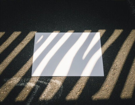 Blank white poster mockup template on asphalt with hard linear shadows