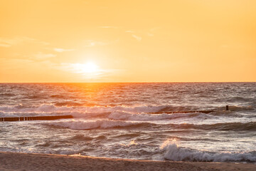 Obraz premium Sunset over the stormy Baltic Sea, high waves over the breakwater, view from the sandy beach.