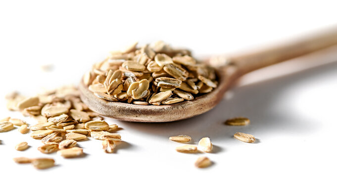Wooden spoon heaped with raw oats and scattered oat flakes on white background closeup,