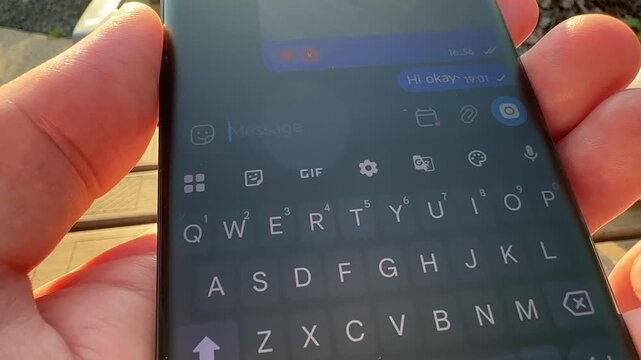 Point of view shot of person holding smartphone and writing message. POV view of male hands typing on dark mobile touchscreen outdoors. Direct perspective of using messaging app on black