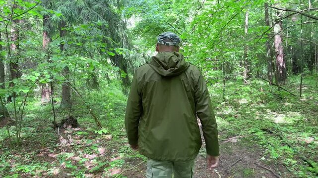 Man striding quickly through the forest from behind. Rear view showing a brisk pace along a wooded path. Active nature walk captured in a green outdoor setting..