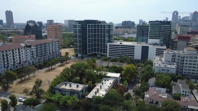 Vast cleared tract borders contemporary glass corporate complexes near Cedar Springs Road, Dallas. Paved neighborhood avenues intersect verdant urban canopies, DFW Metropolitan Area, Texas