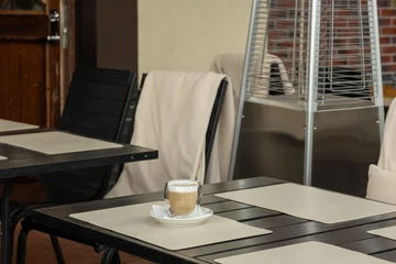 Fotobehang Horeca Cup of coffee on table in outdoor cafe with patio heater during daytime  © Anastasiia