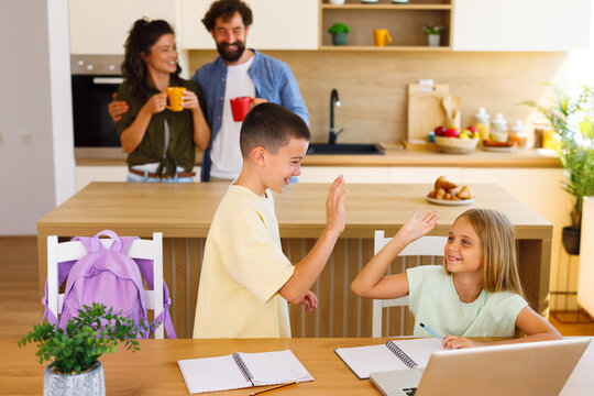 Two siblings celebrating with a high five while doing homework together at the kitchen table