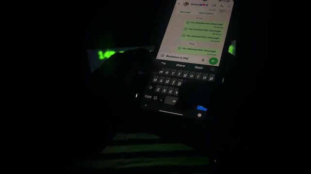 A smartphone with a messaging interface positioned beside a computer keyboard in a dark environment with green digital illumination. The composition highlights online messaging, social media