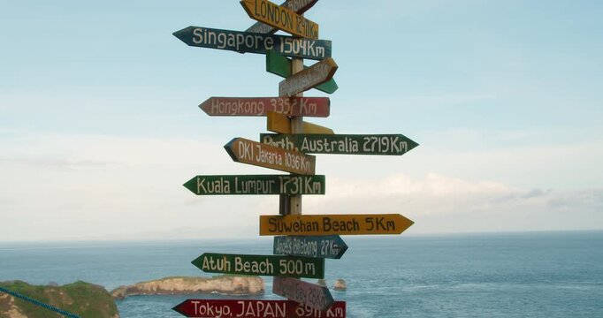 Colorful wooden signpost indicates directions to Singapore and Tokyo at Nusa Penida Bali seaside overlook