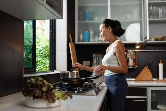 A healthy senior woman cooks a nutritious meal in a modern home kitchen with natural daylight. The authentic lifestyle scene promotes healthy aging, wellness, and everyday home cooking