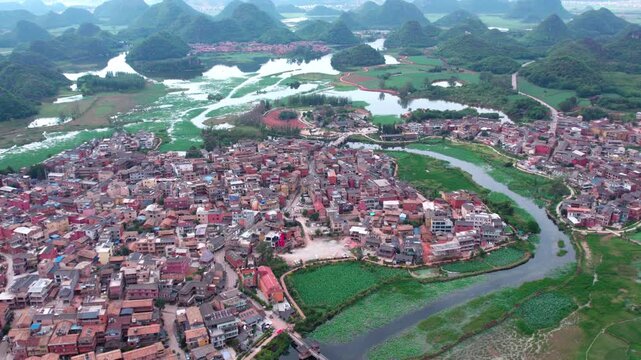 An aerial shot shows a clustered town nestled among karst mountains, winding rivers and green fields.