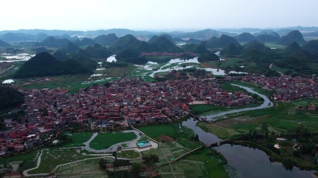 Aerial perspective of a traditional village nestled among karst mountains, with winding rivers and farmlands surrounding it.