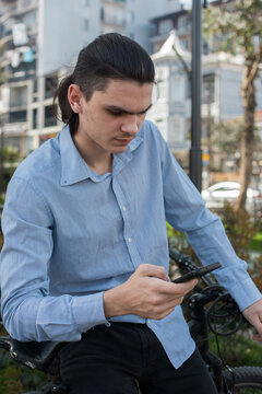 A young man with long hair sits on a bike in a city area.