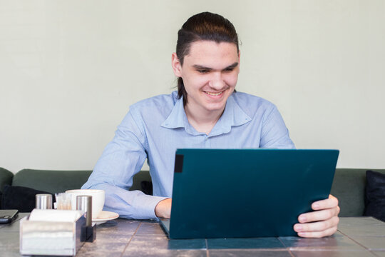 A man takes a break from working on his laptop while sitting in a cafe. He holds a cup of coffee and gazes towards the ceiling.