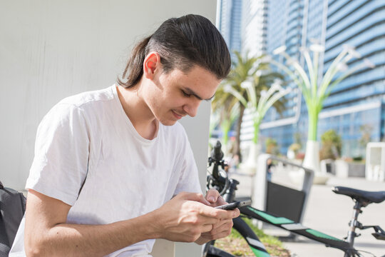 A young man is seated on a bench looking at his phone with focus.