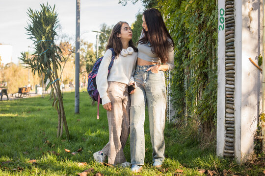 Mother with teenager walk together on a sunny day in a park near a green space with trees and grass