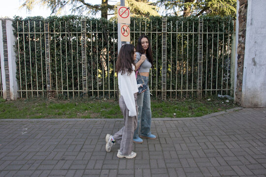 Friends walk together on a sunny day near a park in an urban area discussing their plans for the weekend