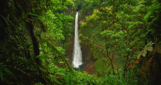 Tall Costa Rica waterfall viewed through lush green jungle foliage on a misty day