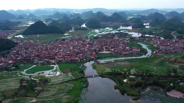 Aerial landscape of a riverside village surrounded by karst mountains and wetland areas.
