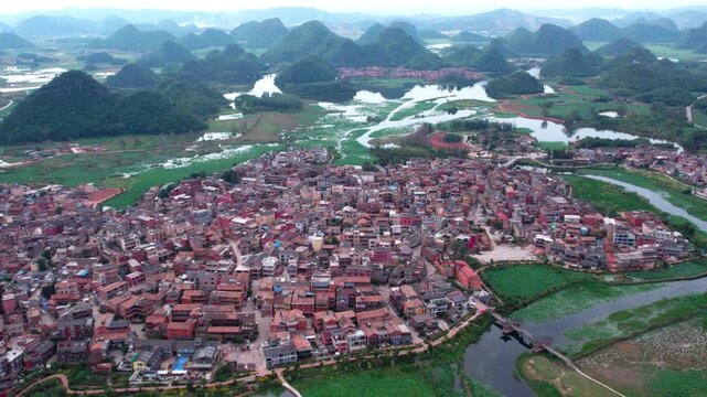 An aerial panorama shows a riverside town surrounded by karst mountains and wetland landscapes.