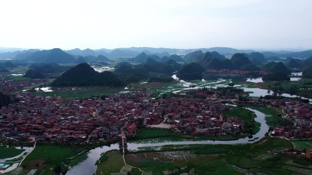 Aerial view of a riverside rural settlement nestled among karst mountains and green farmlands.
