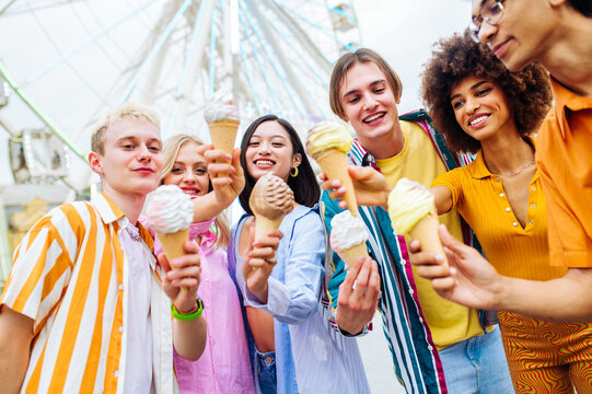 Multiracial young people together meeting at amusement park and eating ice creams - Group of friends with mixed races having fun outdoors - Friendship and lifestyle concepts