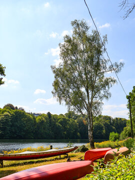 WUPPERTAL, GERMANY - JULY 25, 2026: Red canoes parked on the grassy shore of Beyenburger Stausee reservoir lake on a sunny summer day. .