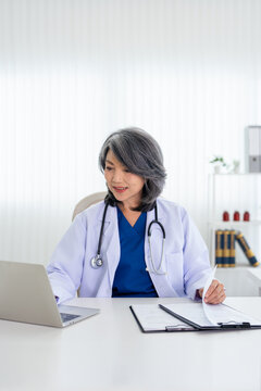 Professional  doctor wearing doctor gown taking notes in medical journal, filling documents, patient illness history, looking at laptop screen.