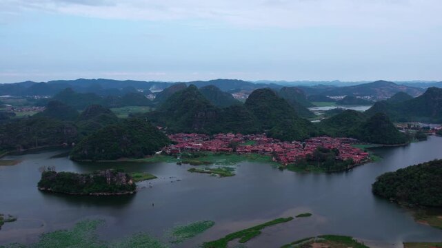 Aerial landscape of a red-roofed village surrounded by lakes and forested karst mountains.