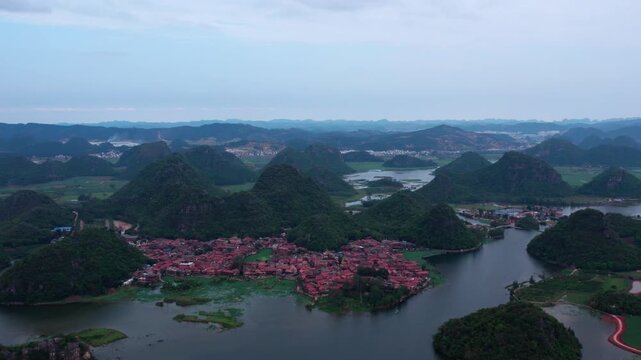 Aerial panorama of a karst landscape featuring water bodies, forested peaks, and a red-roofed village nestled among hills.