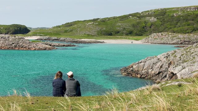 A couple sitting above the turquoise water and sandy beaches of the Isle of Mull, Scotland