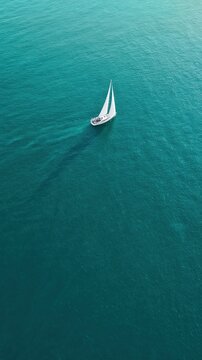 A lone white sailing yacht glides over turquoise sea in a minimalist aerial view. Strong negative space evokes freedom, luxury travel, and serene solitude.
