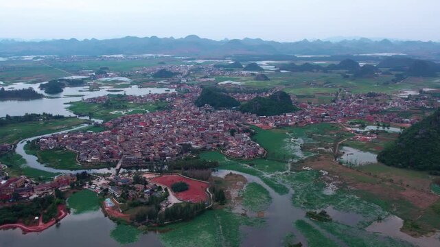 Aerial shot of a riverside village nestled among karst mountains and wetland landscapes.