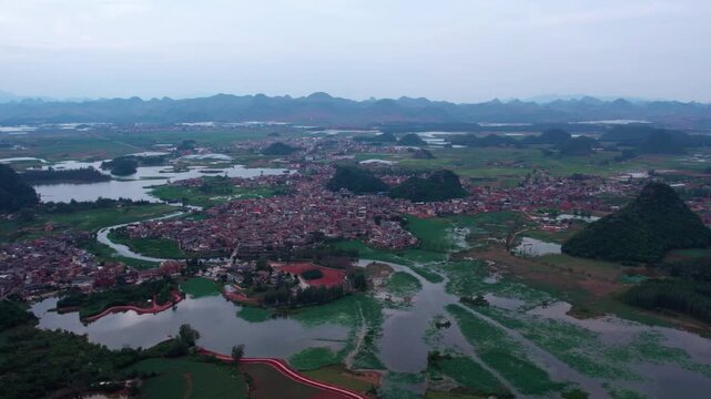 Aerial landscape of a rural settlement surrounded by lakes and karst hills under an overcast sky.