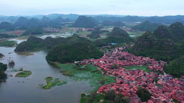 Aerial view of a red-roofed village nestled among karst mountains and calm water bodies.