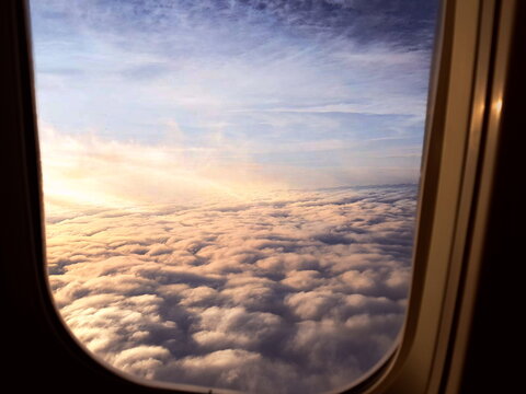 Airplane window view of a sea of clouds at sunset or sunrise, frame-in-frame aerial photography