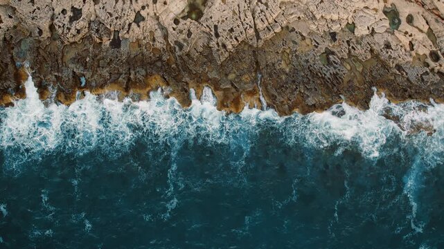 Aerial view of rocky shoreline with foamy waves crashing at the edge