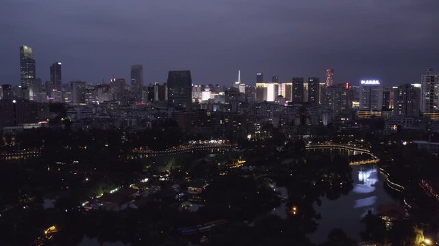 A nighttime panoramic view of an urban cityscape with lit buildings and water features reflecting lights under a dark sky.