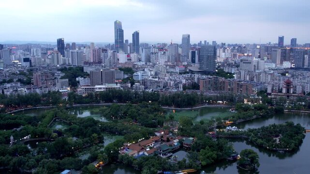 A high-angle aerial view of a metropolitan city, featuring dense urban buildings and a large urban park with water bodies.