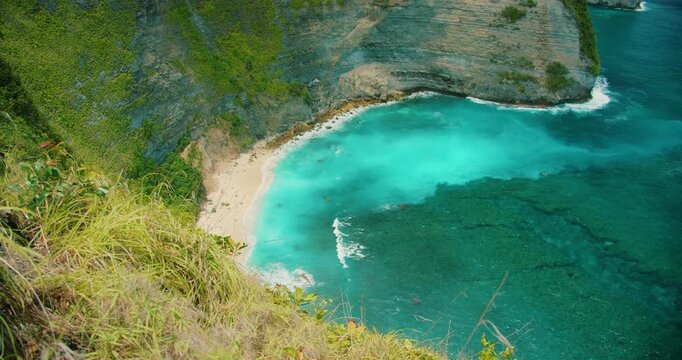 Turquoise ocean water hits white sand beach below steep cliffs in Indonesia
