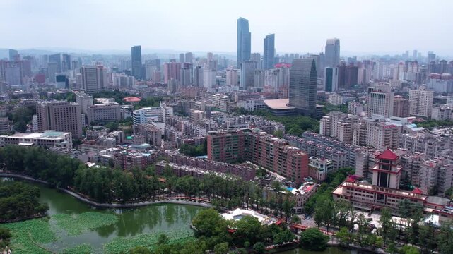 A panoramic aerial view of a dense urban city with a lake and green spaces in the foreground, surrounded by various buildings.