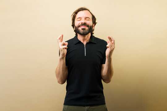 Happy man crossing fingers hoping for good luck and making a wish with eyes closed expressing positive expectation