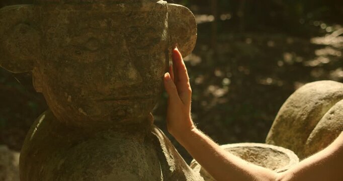 Close-up of hand touching ancient stone statue in tropical forest, highlighting historical craftsmanship in Mexico Yucatan peninsula