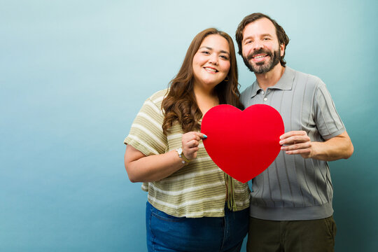 Cheerful couple holding a red heart shape, expressing love and affection on a romantic holiday
