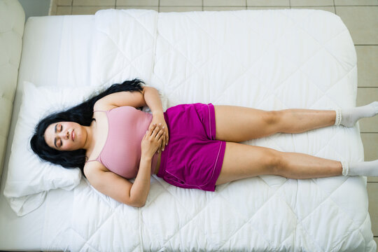 Top view of a woman sleeping soundly in bedroom, resting on white bed during weekend, finding peaceful relaxation and comfort