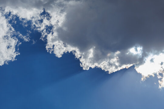 Dramatic view of fluffy white and dark storm clouds against a deep blue sky with bright sunlight breaking through from behind