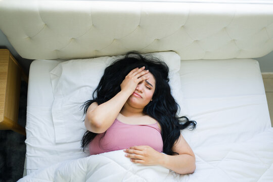 Young woman suffering from a severe headache or migraine in bed, covering her eyes and experiencing pain and exhaustion