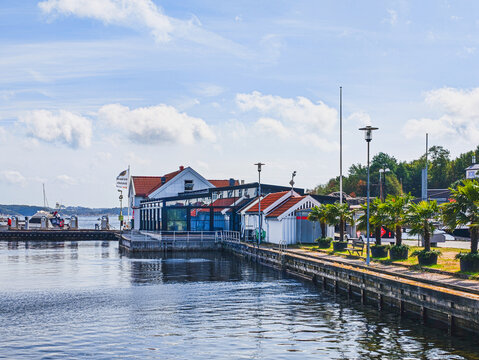 KRISTIANSAND, NORWAY - AUGUST 9, 2026: Waterfront marina with boats, traditional coastal buildings and a promenade in Kristiansand on a sunny summer day.